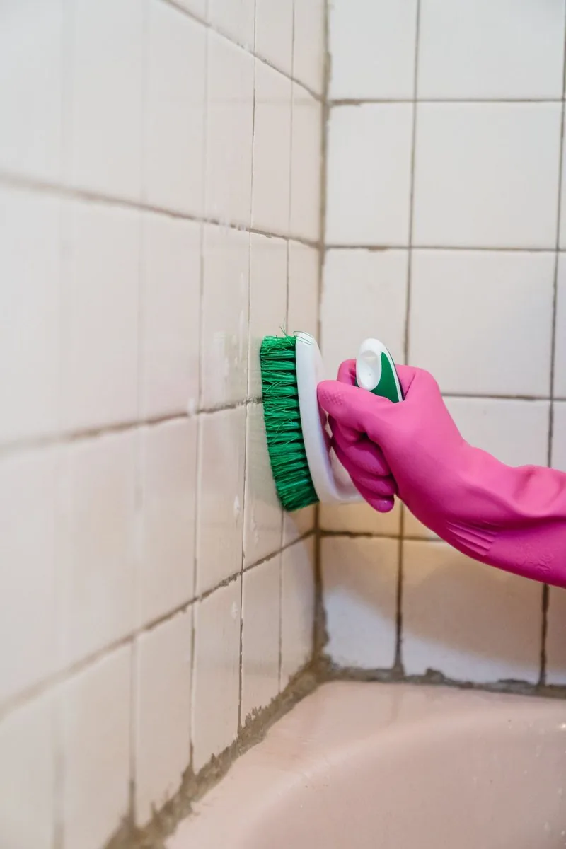 Gloved hand scrubbing tiled surfaces during a deep clean